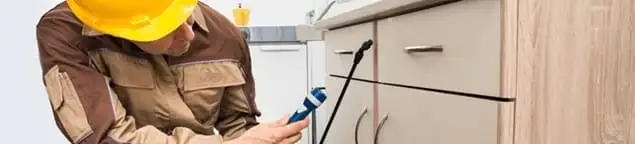 Roach exterminator applying treatment under kitchen cabinets in Fort Collins, CO