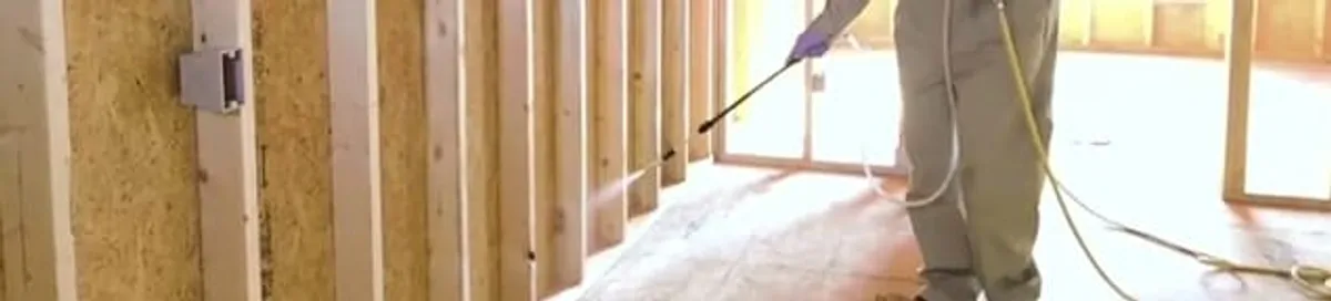 Termite treatment technician applying spray along framing and unfinished walls in Fort Collins, CO